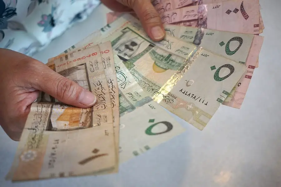 امرأة تحمل أوراق عمل بالريال السعودي