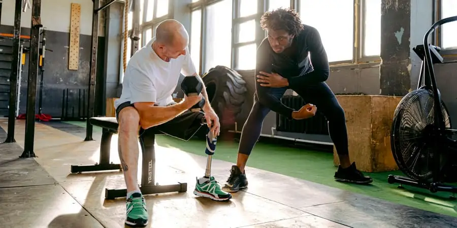 fitness instructor guides a man with a prosthetic leg through weight training