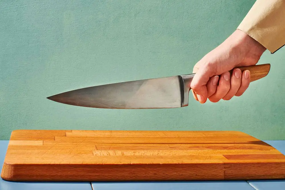 شخص يحمل سكين طاه فوق لوح تقطيع خشبي