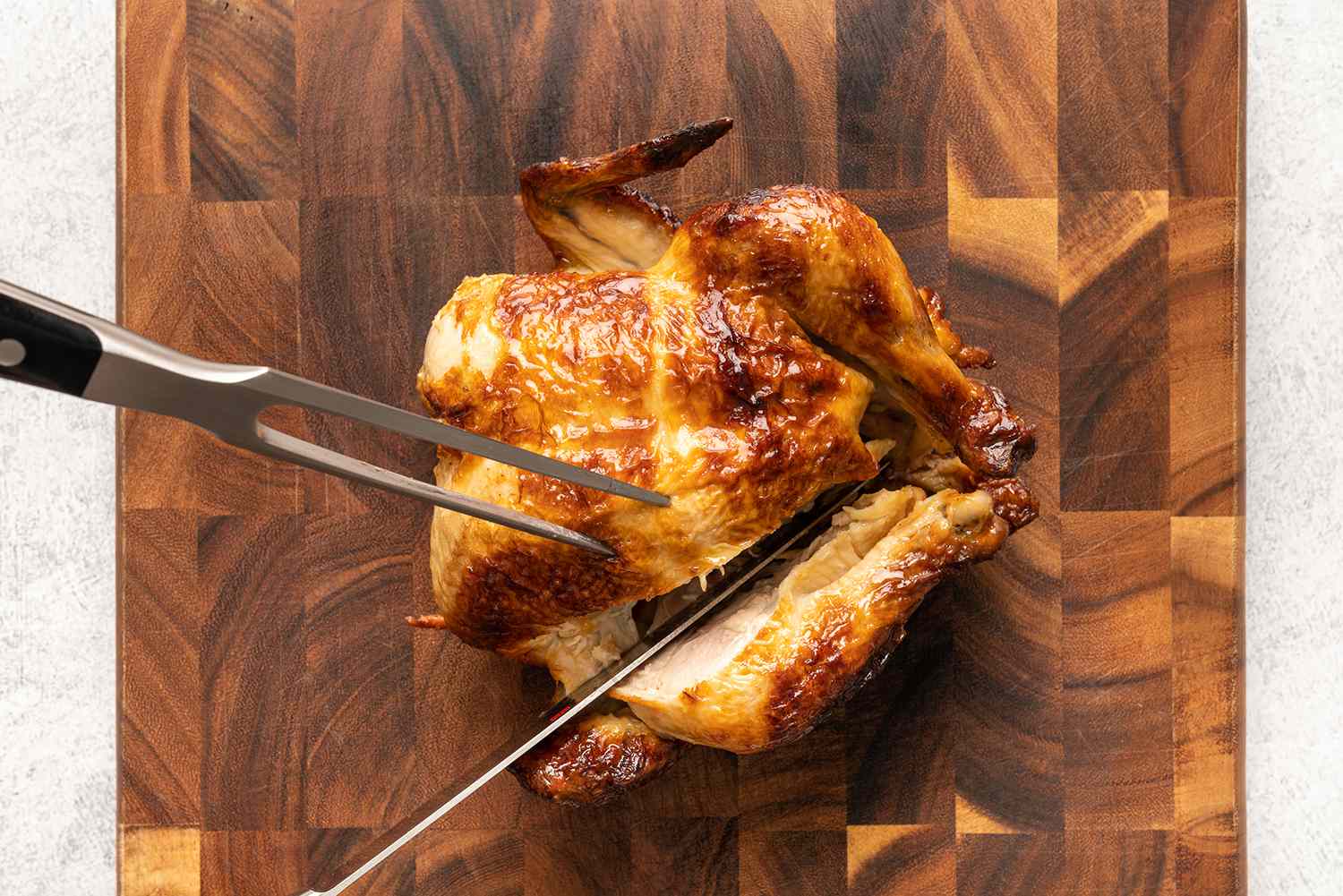 دجاج مشوي كامل يتم نحته على لوح تقطيع ، قطع سكين إلى ساق منفصلة عن الصدر