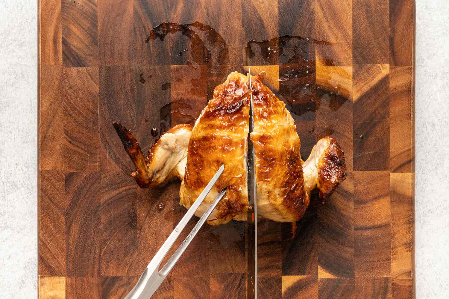 صدر دجاج مشوي كامل وأجنحة على لوح التقطيع ، سكين يقطع العمود الفقري لتقطيع لحم الصدر إلى قطعتين